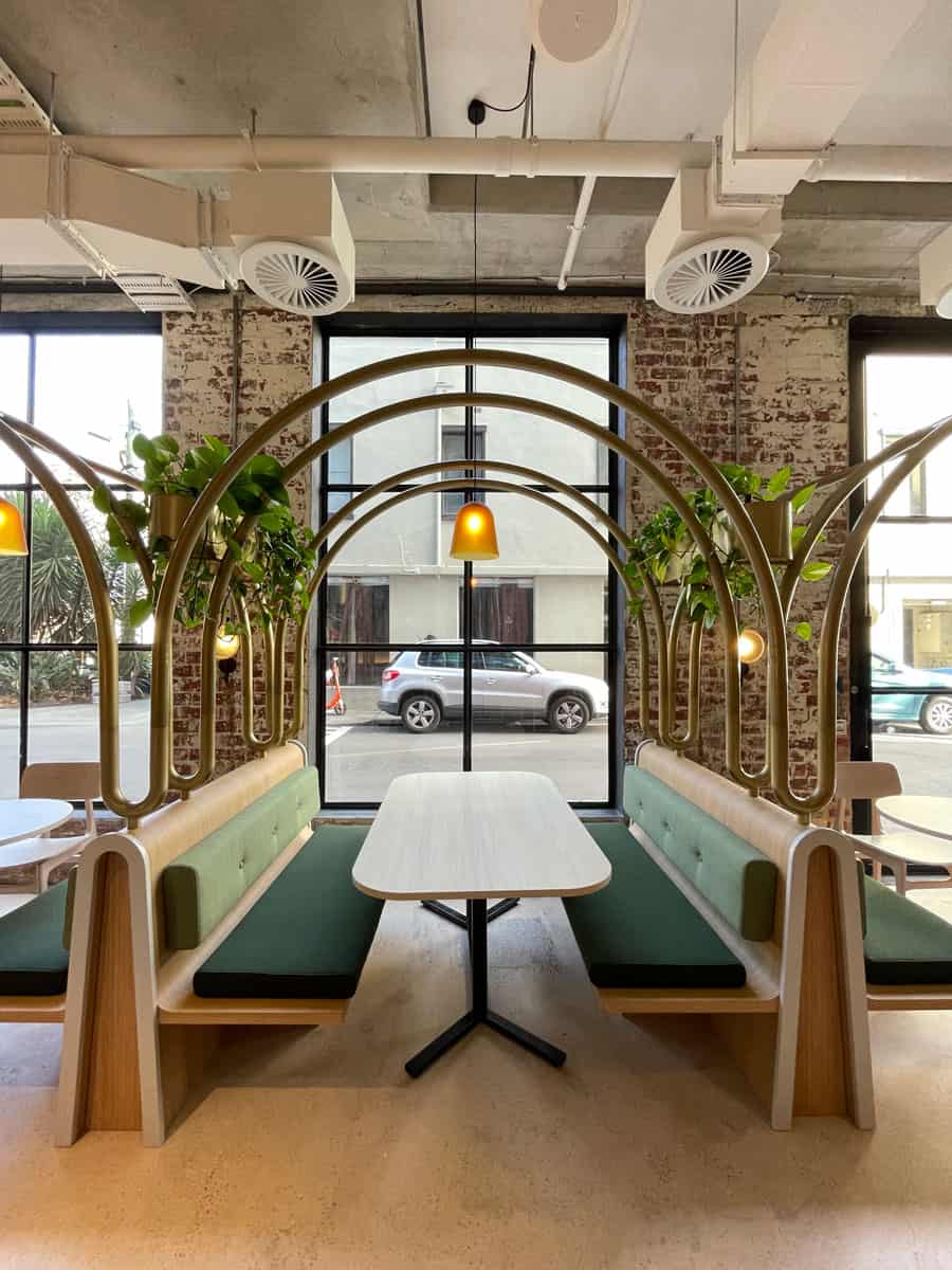 Plants hanging amongst arches in green and oak timber dining space